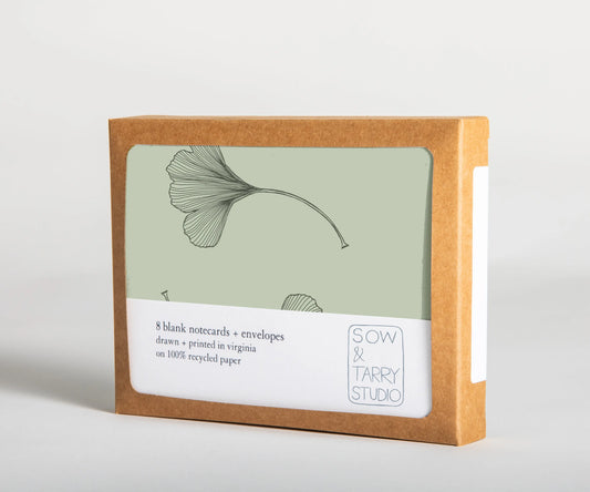 A boxed set of blank notecards, printed with a hand-drawn illustration of a gingko leaf pattern on green uncoated, recyclable paper. Packaged in a compostable box.
